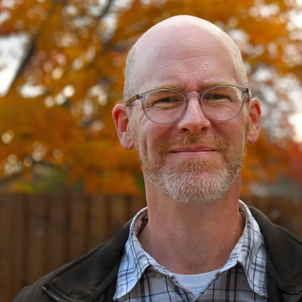 A photo of Joe Wells, in front of a tree with fall colors